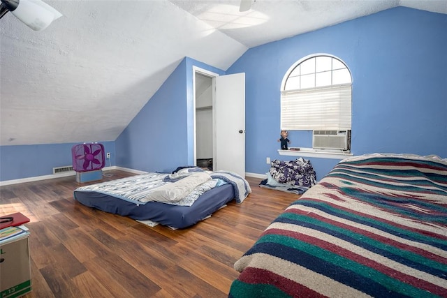 bedroom with ceiling fan, vaulted ceiling, dark hardwood / wood-style floors, cooling unit, and a textured ceiling