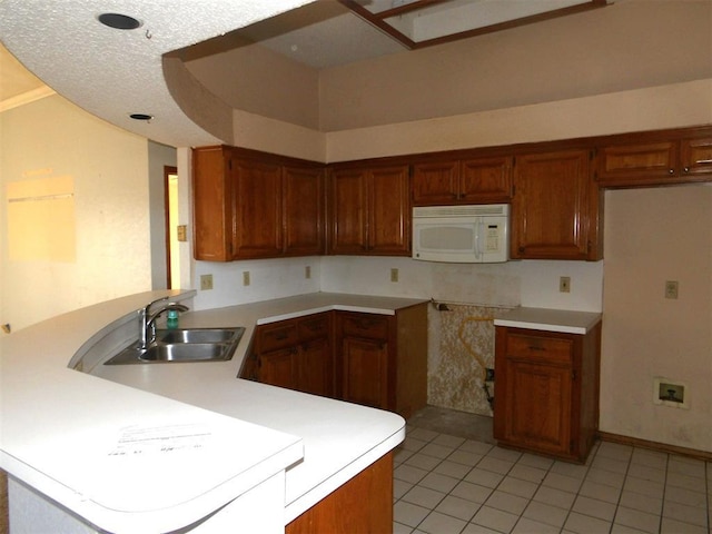 kitchen featuring a textured ceiling, light tile patterned floors, kitchen peninsula, and sink