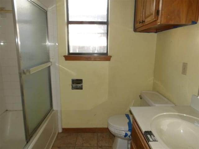 full bathroom with tile patterned floors, bath / shower combo with glass door, toilet, and vanity