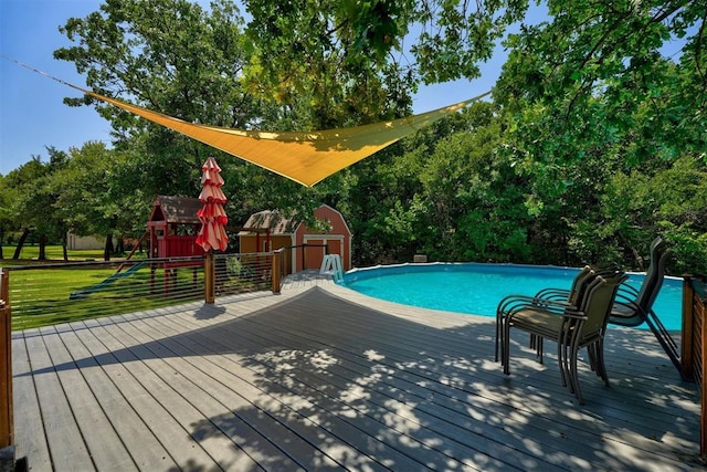 view of swimming pool featuring a playground, a deck, a shed, and a yard