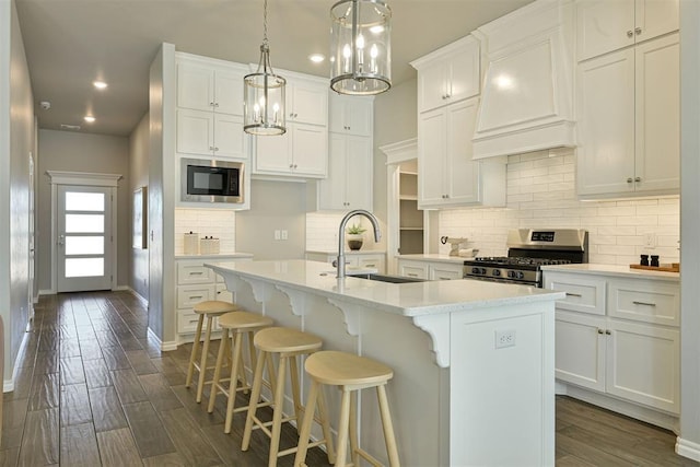 kitchen with stainless steel range, white cabinets, a kitchen island with sink, and built in microwave