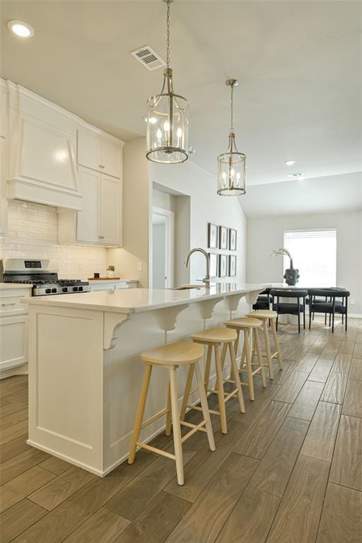 kitchen with stainless steel stove, white cabinets, a kitchen breakfast bar, hanging light fixtures, and a kitchen island with sink