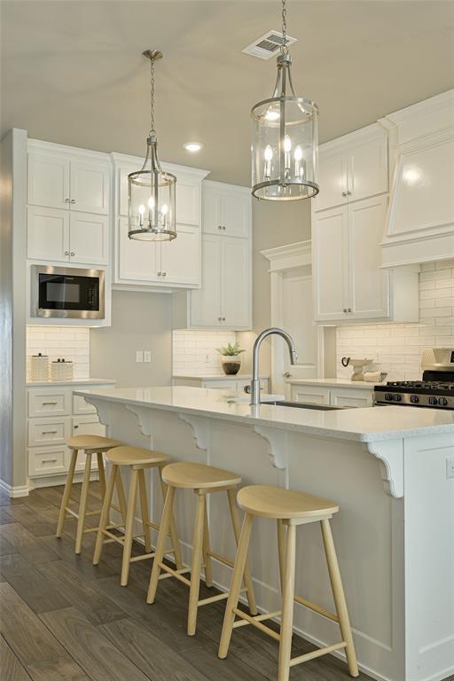 kitchen with built in microwave, stainless steel gas stove, a center island with sink, dark hardwood / wood-style flooring, and white cabinets