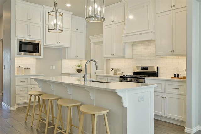 kitchen featuring stainless steel stove, a kitchen island with sink, white cabinetry, built in microwave, and custom exhaust hood