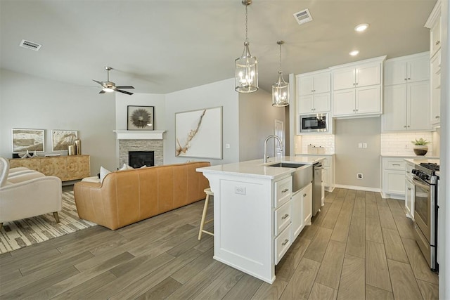 kitchen featuring decorative light fixtures, stainless steel appliances, white cabinets, and a center island with sink