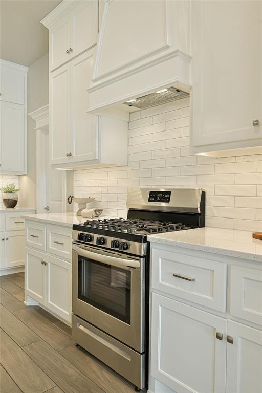 kitchen featuring stainless steel gas range oven, light stone counters, white cabinets, and backsplash