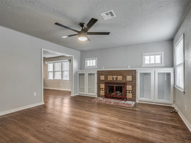 unfurnished living room with ceiling fan, dark wood-type flooring, a textured ceiling, and a brick fireplace