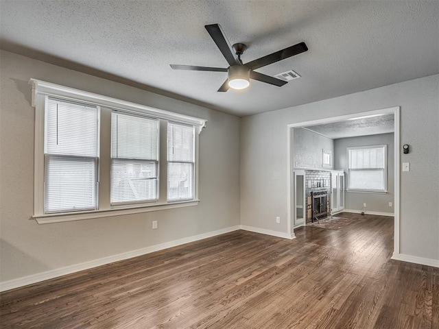 unfurnished living room with ceiling fan, dark hardwood / wood-style floors, a textured ceiling, and a brick fireplace