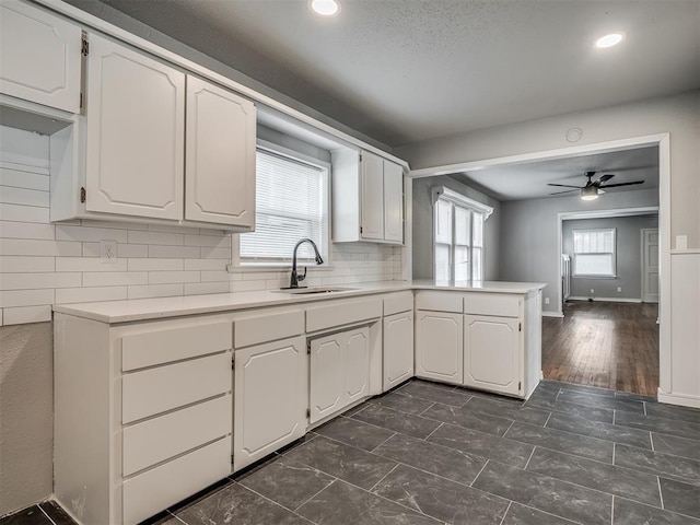 kitchen with kitchen peninsula, decorative backsplash, white cabinets, and sink