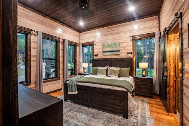 bedroom featuring wood ceiling, light hardwood / wood-style floors, a barn door, and wood walls