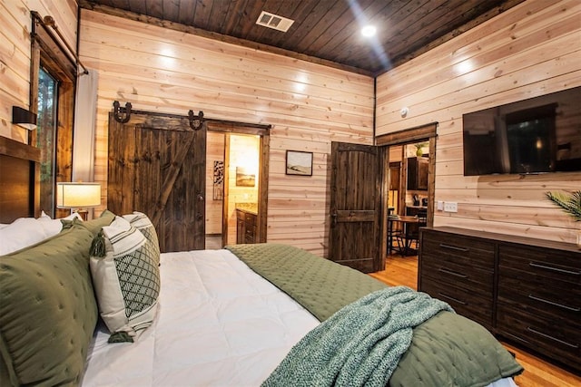 bedroom with a barn door, wood walls, wood ceiling, and light hardwood / wood-style floors