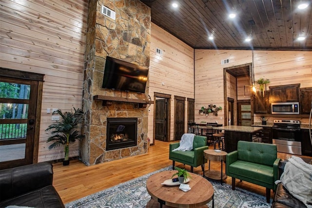 living room featuring wooden walls, visible vents, wood ceiling, light wood-style flooring, and a fireplace