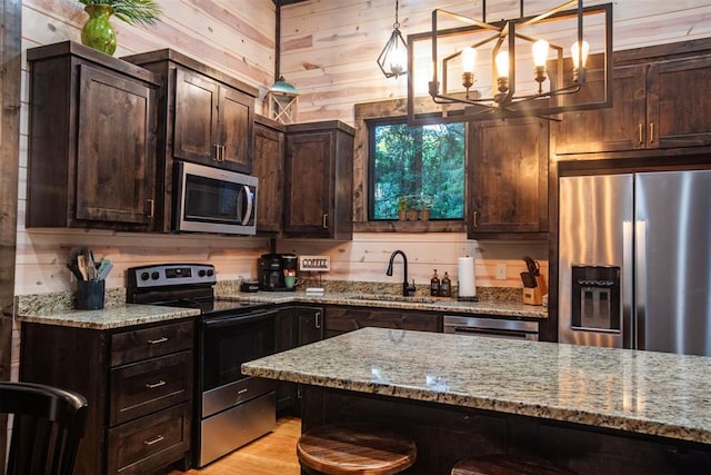 kitchen featuring stainless steel appliances, a sink, wooden walls, and dark brown cabinetry