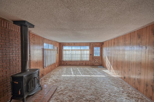 unfurnished living room with light carpet, a textured ceiling, a wood stove, and wooden walls