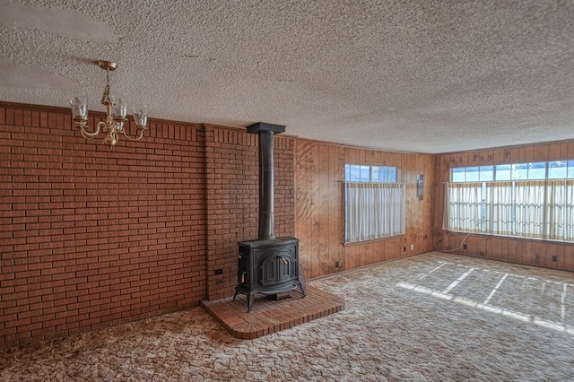 unfurnished living room featuring carpet floors, a wood stove, a textured ceiling, and an inviting chandelier