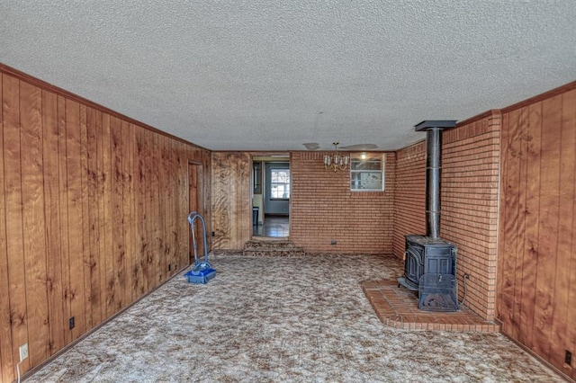 unfurnished living room featuring a wood stove, a textured ceiling, wood walls, and carpet flooring