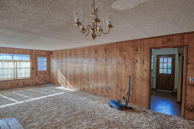 interior space with a wealth of natural light, wood walls, a chandelier, and a textured ceiling