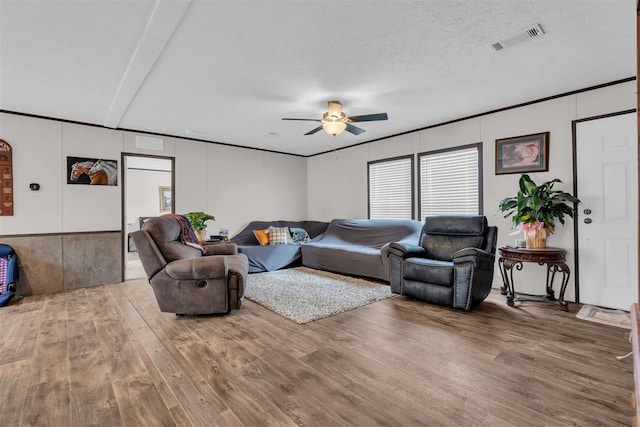 living room with ceiling fan, wood-type flooring, a textured ceiling, crown molding, and beam ceiling