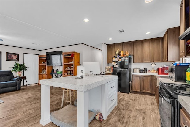 kitchen with a kitchen bar, black appliances, a kitchen island, and light wood-type flooring