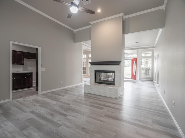 unfurnished living room with ceiling fan, a brick fireplace, ornamental molding, and light hardwood / wood-style floors