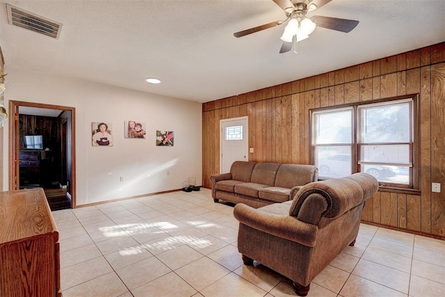 living room featuring ceiling fan, light tile patterned floors, and wooden walls