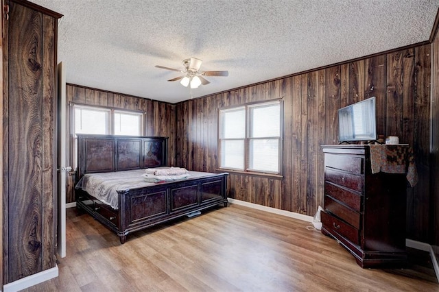 bedroom with a textured ceiling, ceiling fan, light hardwood / wood-style flooring, and wooden walls