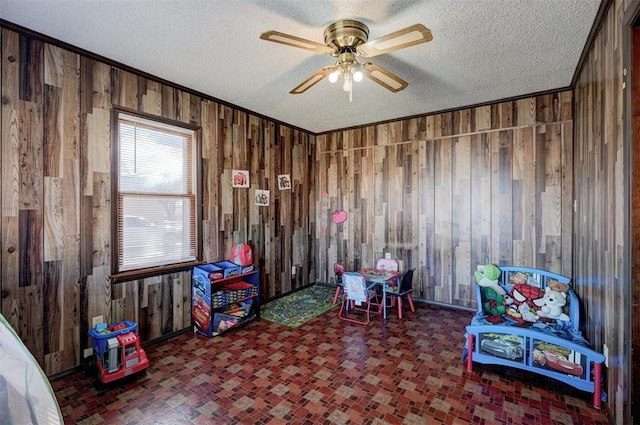 recreation room featuring ceiling fan, a textured ceiling, crown molding, and wooden walls