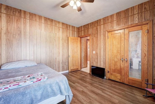 bedroom featuring ceiling fan, hardwood / wood-style floors, and wood walls