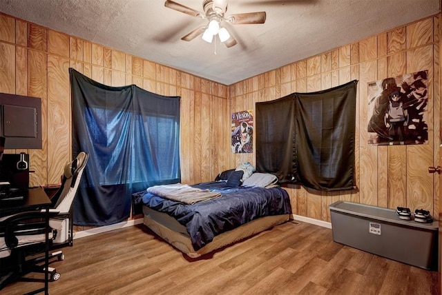 bedroom featuring ceiling fan, a textured ceiling, hardwood / wood-style floors, and wooden walls