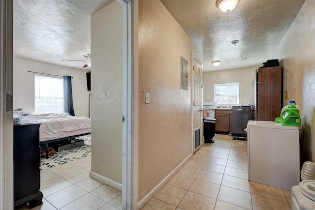 corridor featuring light tile patterned flooring, a textured ceiling, electric panel, and a healthy amount of sunlight