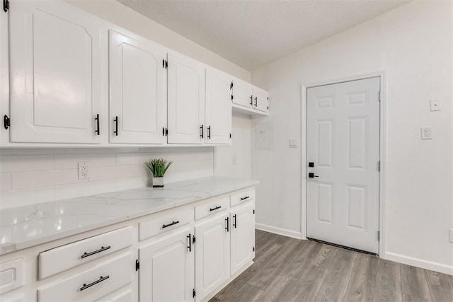 kitchen featuring white cabinetry, decorative backsplash, a textured ceiling, light hardwood / wood-style flooring, and light stone counters