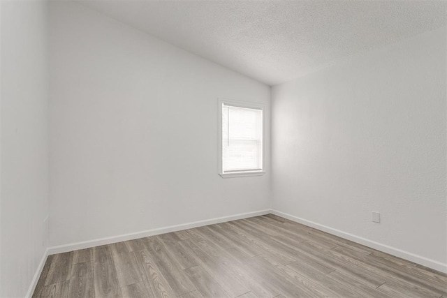 unfurnished room featuring light hardwood / wood-style floors, a textured ceiling, and vaulted ceiling