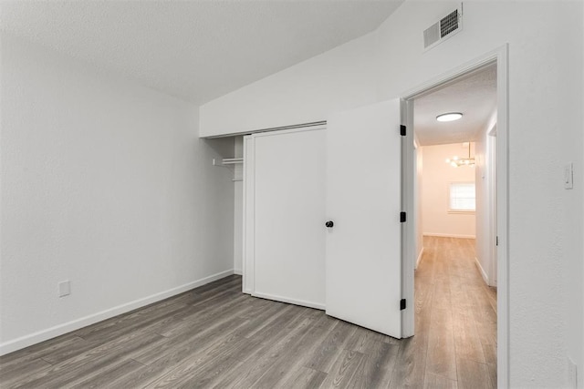 unfurnished bedroom featuring a textured ceiling, lofted ceiling, wood-type flooring, an inviting chandelier, and a closet