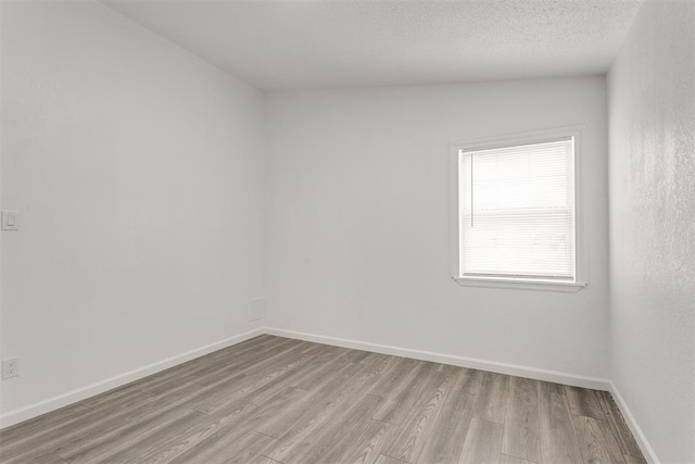 unfurnished room featuring lofted ceiling, light wood-type flooring, and a textured ceiling