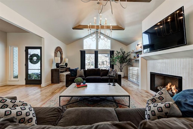 living room featuring an inviting chandelier, a tiled fireplace, light hardwood / wood-style floors, and vaulted ceiling with beams