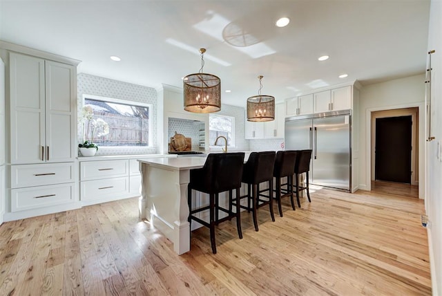 kitchen featuring white cabinetry, a kitchen bar, hanging light fixtures, stainless steel built in fridge, and a center island with sink