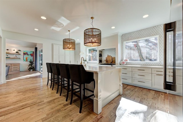 kitchen featuring a breakfast bar area, decorative light fixtures, light hardwood / wood-style flooring, a kitchen island with sink, and white cabinets