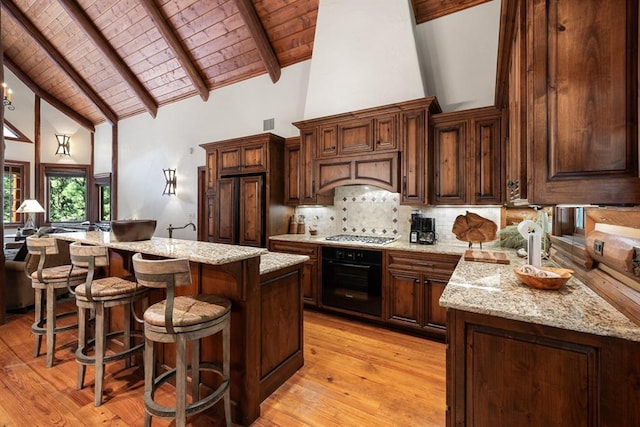 kitchen with black oven, a breakfast bar area, a center island, light stone countertops, and wooden ceiling