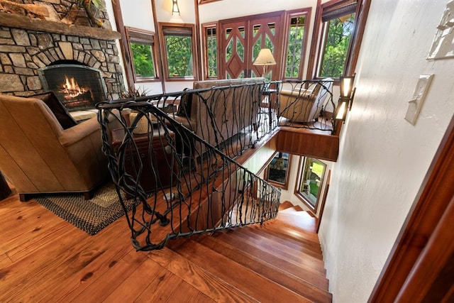 staircase featuring a stone fireplace, wood-type flooring, and a healthy amount of sunlight