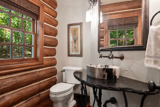 bathroom with sink, log walls, and toilet