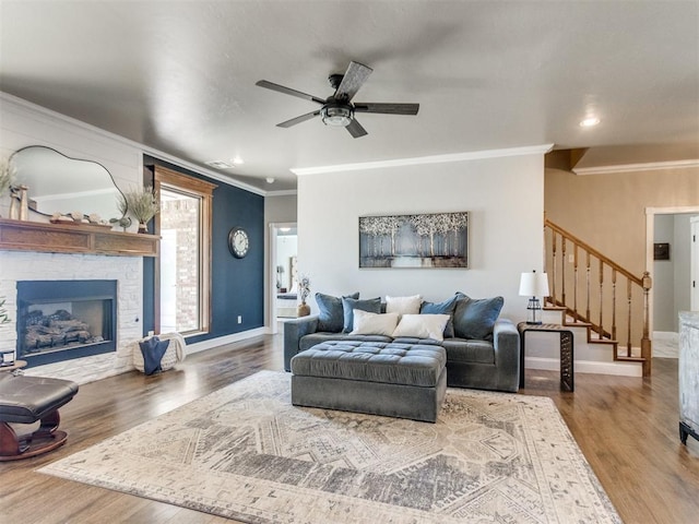 living room featuring ceiling fan, hardwood / wood-style floors, ornamental molding, and a large fireplace