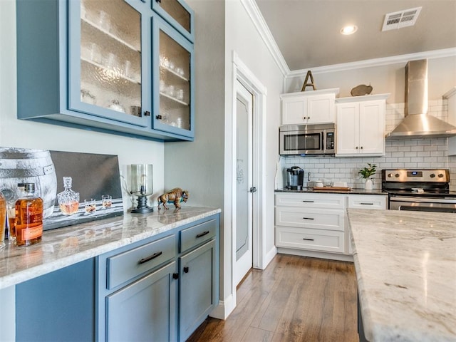 kitchen with crown molding, appliances with stainless steel finishes, backsplash, white cabinets, and wall chimney range hood