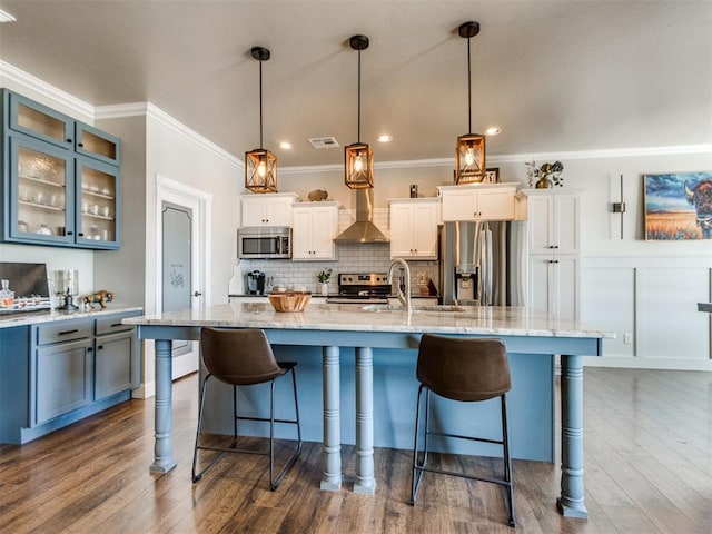 kitchen featuring decorative light fixtures, white cabinets, wall chimney exhaust hood, and appliances with stainless steel finishes