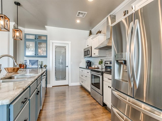 kitchen with white cabinets, appliances with stainless steel finishes, wall chimney range hood, sink, and hanging light fixtures