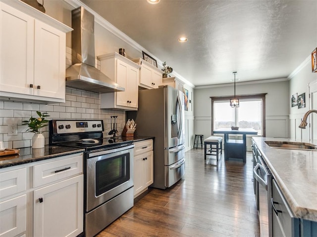 kitchen with hanging light fixtures, appliances with stainless steel finishes, wall chimney exhaust hood, sink, and white cabinetry