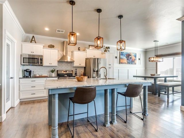 kitchen featuring wall chimney range hood, decorative light fixtures, appliances with stainless steel finishes, and a spacious island