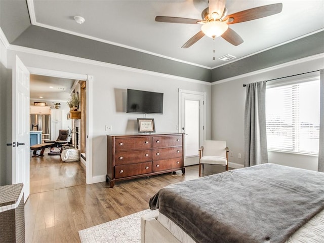 bedroom with light hardwood / wood-style flooring, a tray ceiling, ceiling fan, and ornamental molding