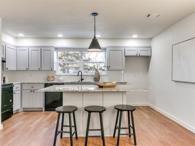 kitchen with pendant lighting, black dishwasher, a center island, light stone counters, and light hardwood / wood-style floors