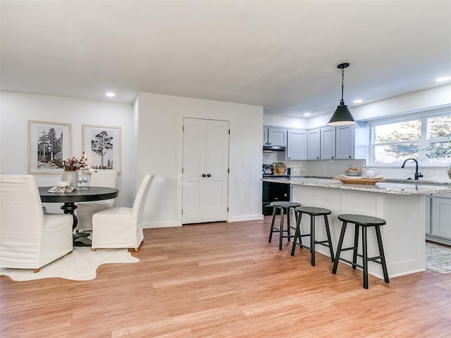 kitchen with hanging light fixtures, a breakfast bar, sink, and light hardwood / wood-style floors