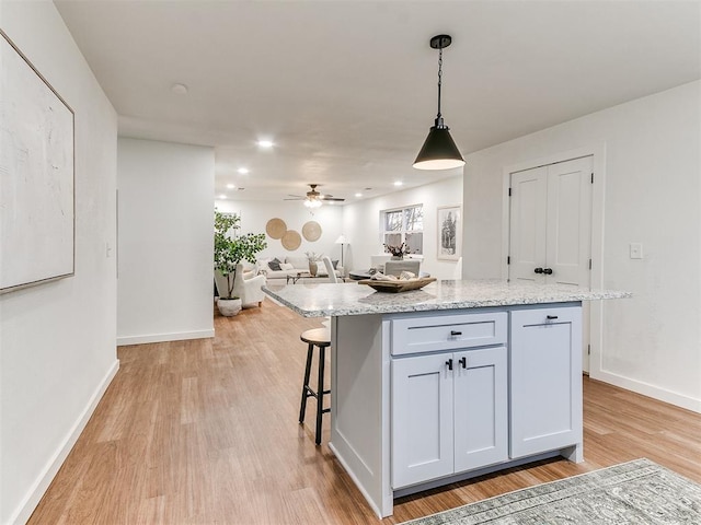 kitchen featuring pendant lighting, light stone countertops, a center island, and ceiling fan